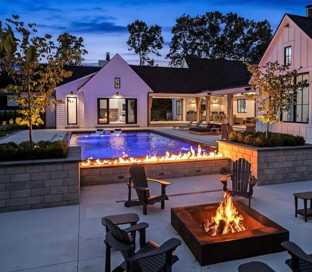 Backyard pool and fire pit glowing at dusk behind a white house