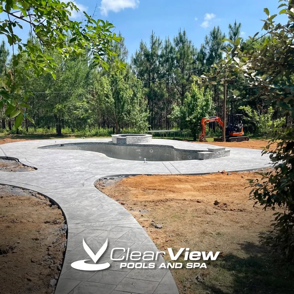 Newly finished curved pool and stamped deck among pine trees