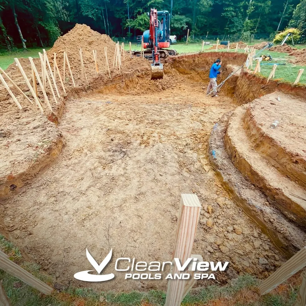 Freshly excavated pool shape with steps and an excavator at work