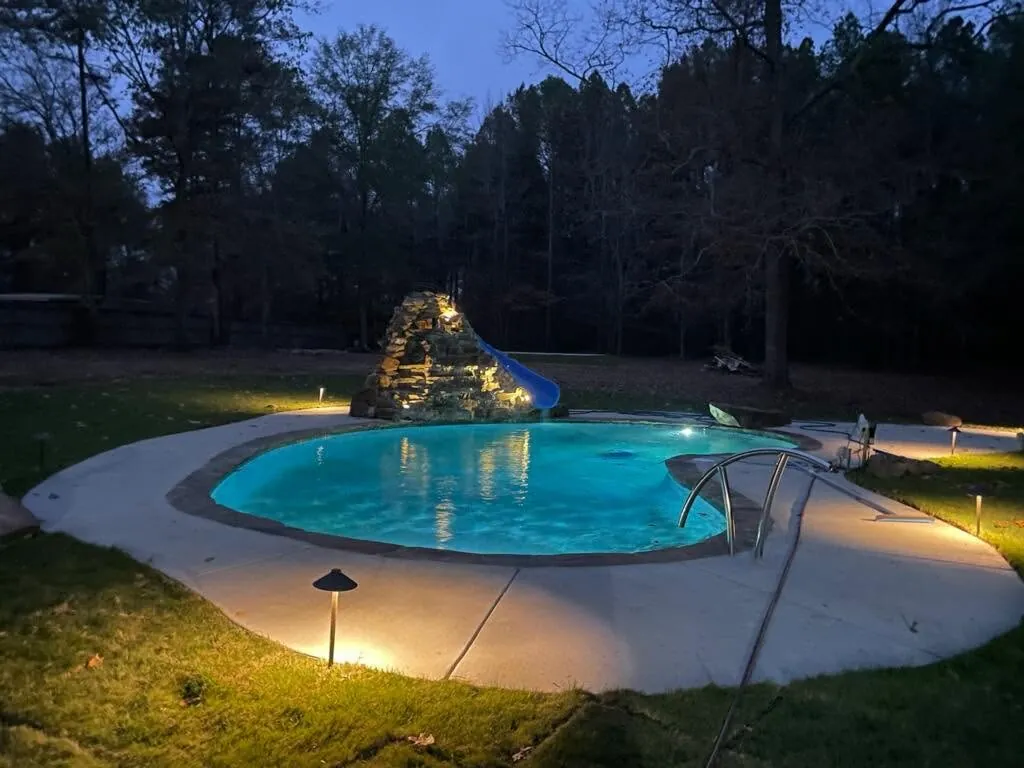 Backyard pool with a slide and lights glowing at night